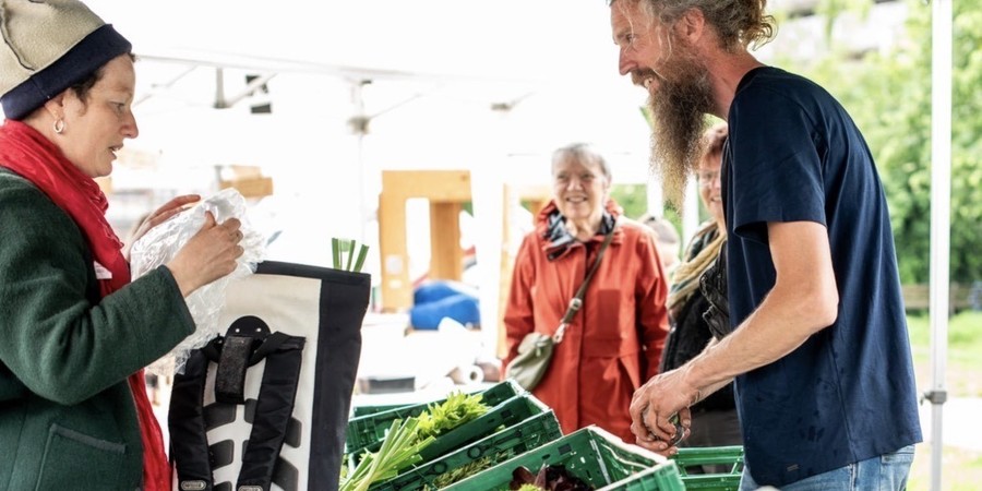 Foto van boer met groenenkraam en Borgerhoutse klant: Boerenmarkt Borgerhout keert terug naar het Vinçotteplein voor 5 opeenvolgende edities