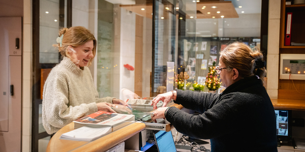 Een vrouw staat aan de balie en wisselt een document uit
