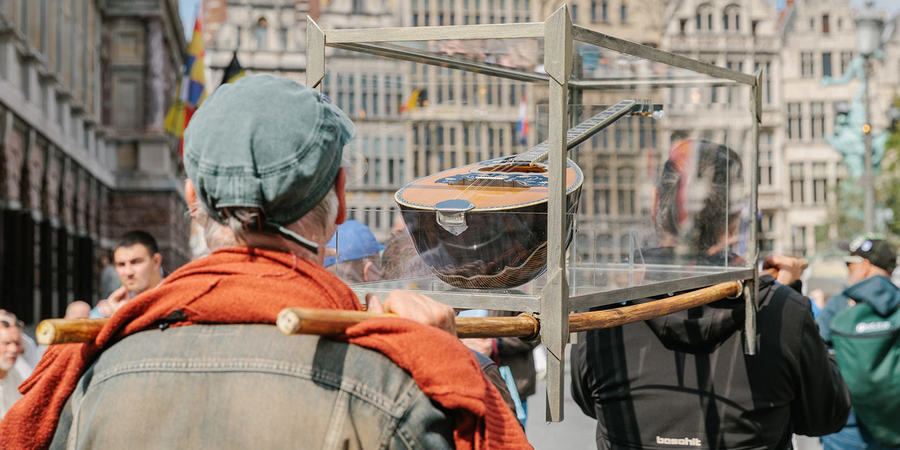 2 mannen dragen glazen kist met muziekinstrument
