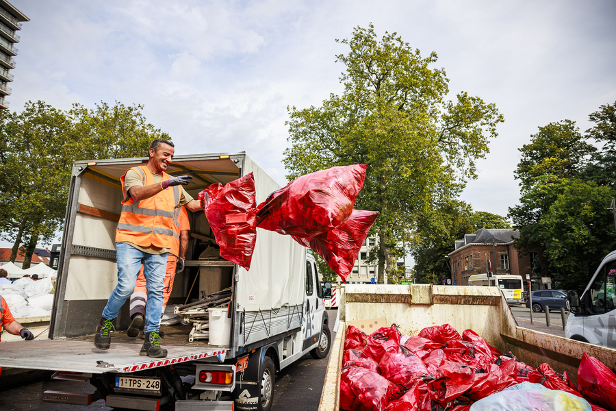 Een man gooit een rode zak met zwerfvuil in een afvalcontainer.