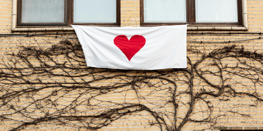 Witte doek met een rood, geschilderd hart hangt uit het bovenraam van een huis Witte doek met een rood, geschilderd hart hangt uit het bovenraam van een huis