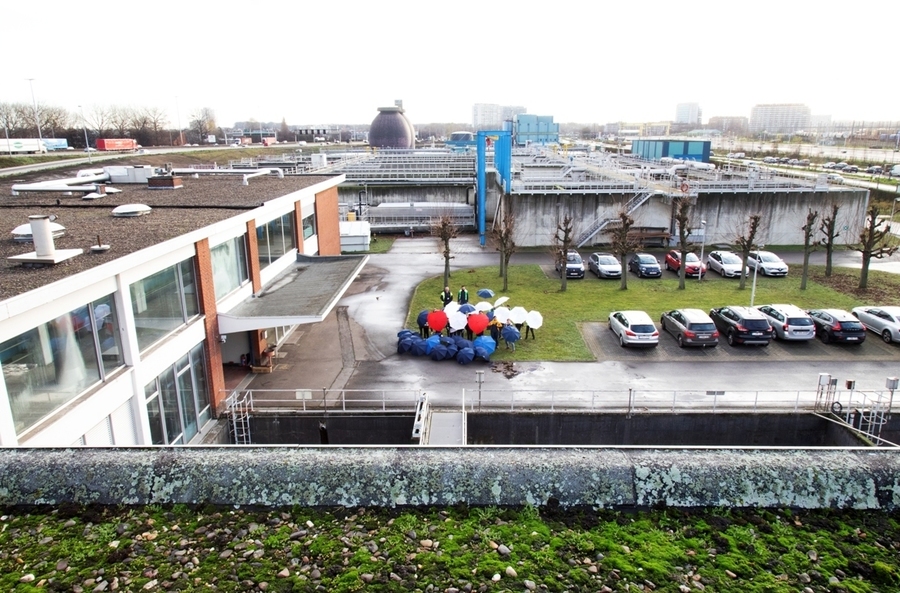 Foto vanop het dak van Aquafin dat helaas niet geschikt is voor een klimaatrobuust dak. De medewerkers van Aquafin houden een paraplu vast op de begane grond. Foto vanop het dak van Aquafin dat helaas niet geschikt is voor een klimaatrobuust dak. De medewerkers van Aquafin houden een paraplu vast op de begane grond.