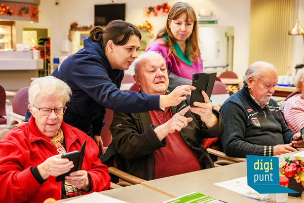 Oudere personen worden geholpen met het gebruik van hun smartphone.