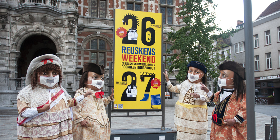 Vier Reuskens staan rond een bord met praktische info over het Reuskensweekend. Op de achtergrond het districtshuis van Borgerhout.