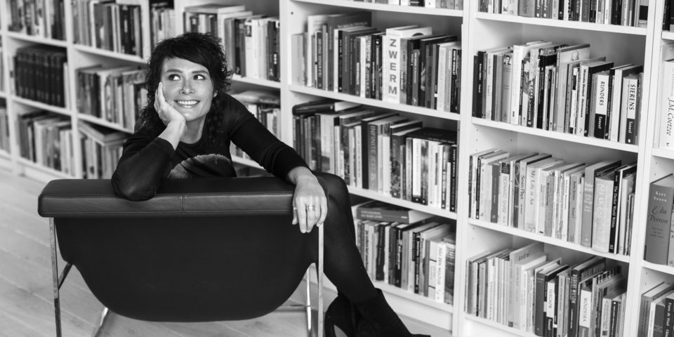Schrijfster Griet Op de Beeck op een zwarte zeten vóór een boekenrek