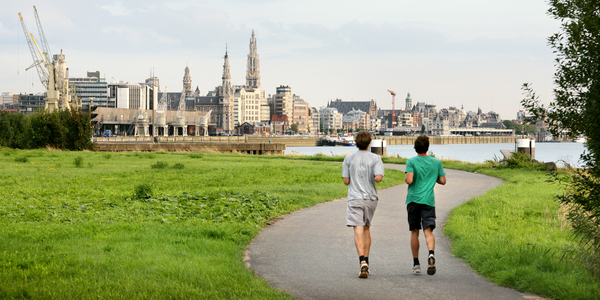 2 joggers lopen zij aan zij aan de Scheldekaaien met panoramisch zicht op de Antwerpen en de kathedraal
