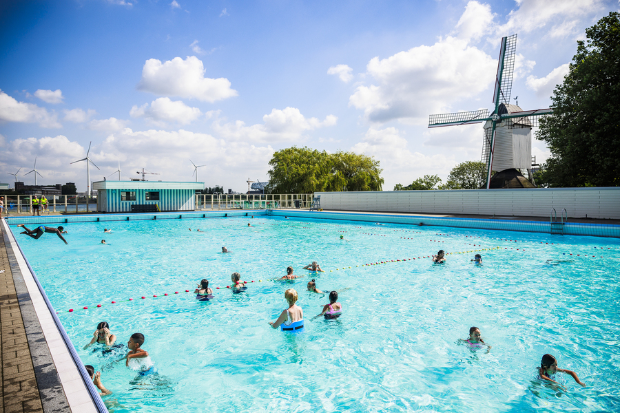 Beeld van het grote bad van openluchtzwembad De Molen met op de achtergrond de molen die het bad zijn naam gaf