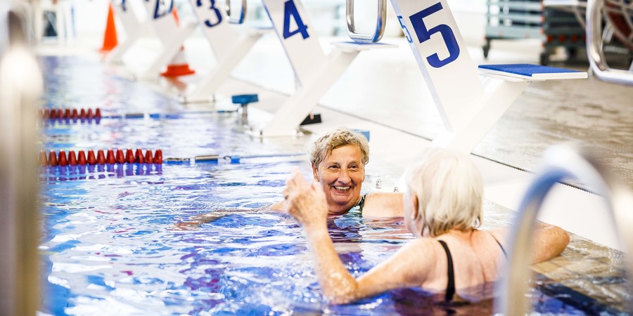 Twee dames hangen vrolijk lachend aan de kant van het zwembad