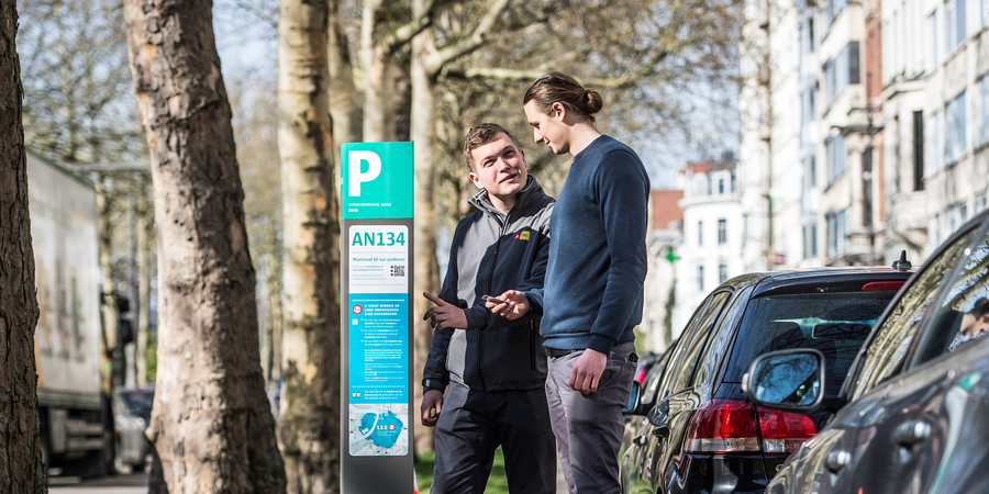 Parkeerwachter en burger staan voor een parkeerautomaat.