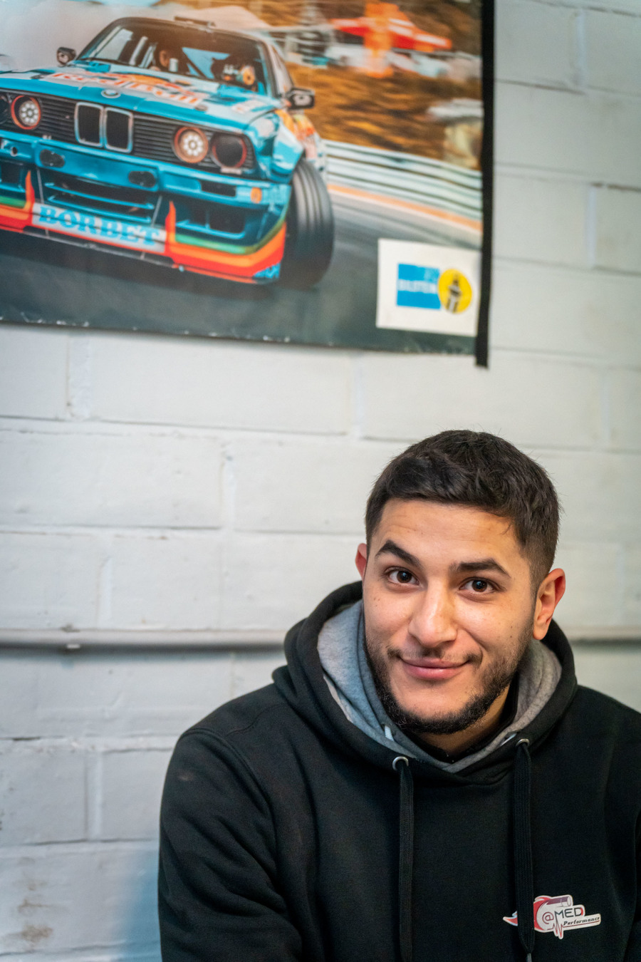 Portret van Hicham onder een poster met sportwagen
