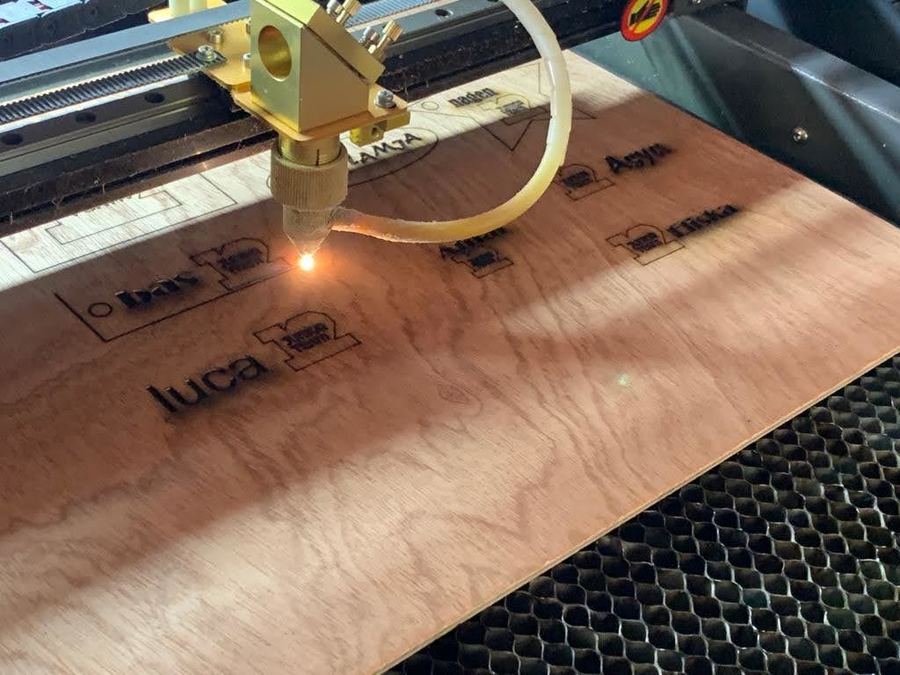 Een lasercutter snijdt de ontworpen sleutelhangers uit een houten plaat.