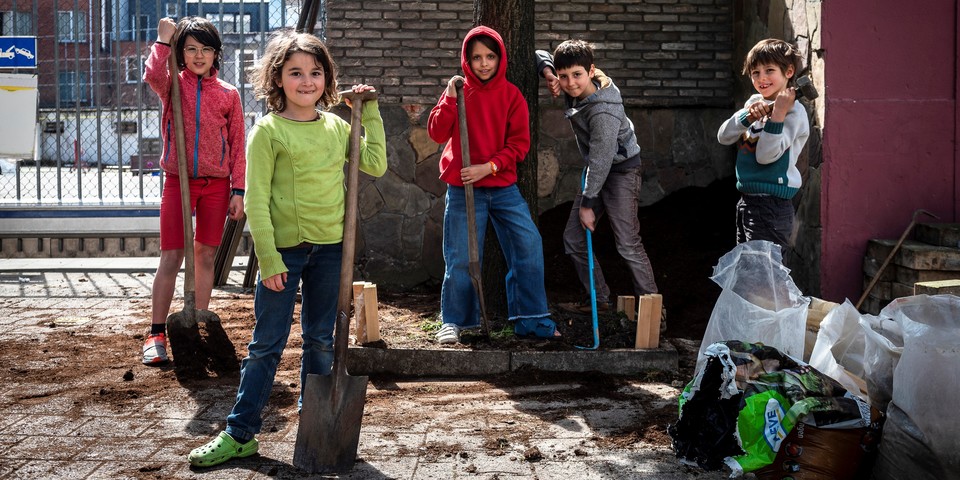Kinderen staan met spades rond een Buurtboom die ze samen aan het aanleggen zijn.