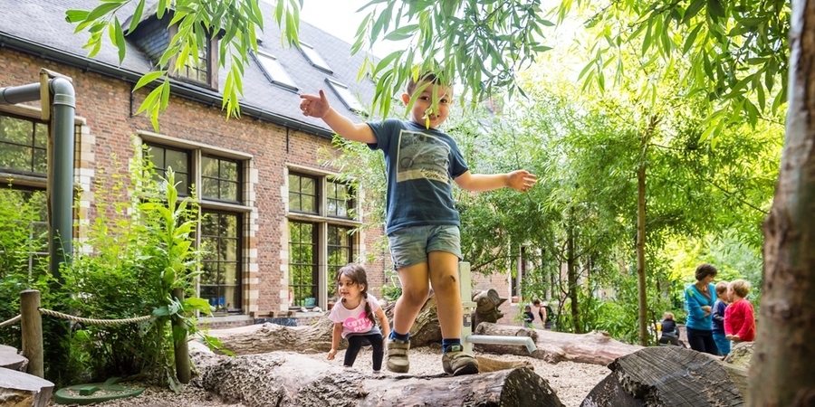 Een jongetje loopt over een boomstam op een klimaatrobuuste natuurspeelplaats