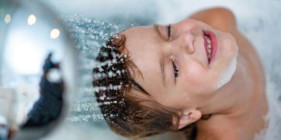 Kind onder de douche laat water op gezicht met gesloten ogen vallen