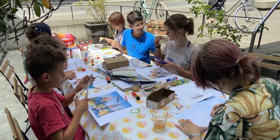 Kinderen knutselen met schaar en papier aan een lange tafel op een terras