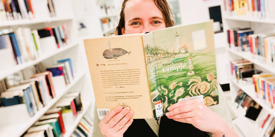 Een bezoeker van de Bibliotheek verstopt zich achter een kinderboek. Een bezoeker van de Bibliotheek verstopt zich achter een kinderboek.