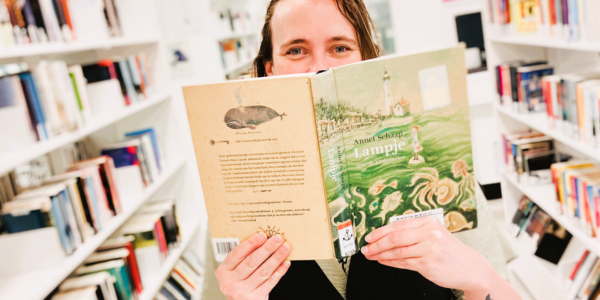 Een bezoeker van de Bibliotheek verstopt zich achter een kinderboek.