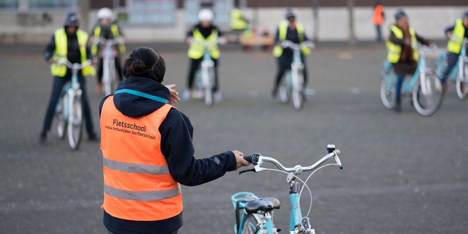 Lesgever van de Fietsschool geeft instructies aan de leerlingen die op de achtergrond op de fiets zitten