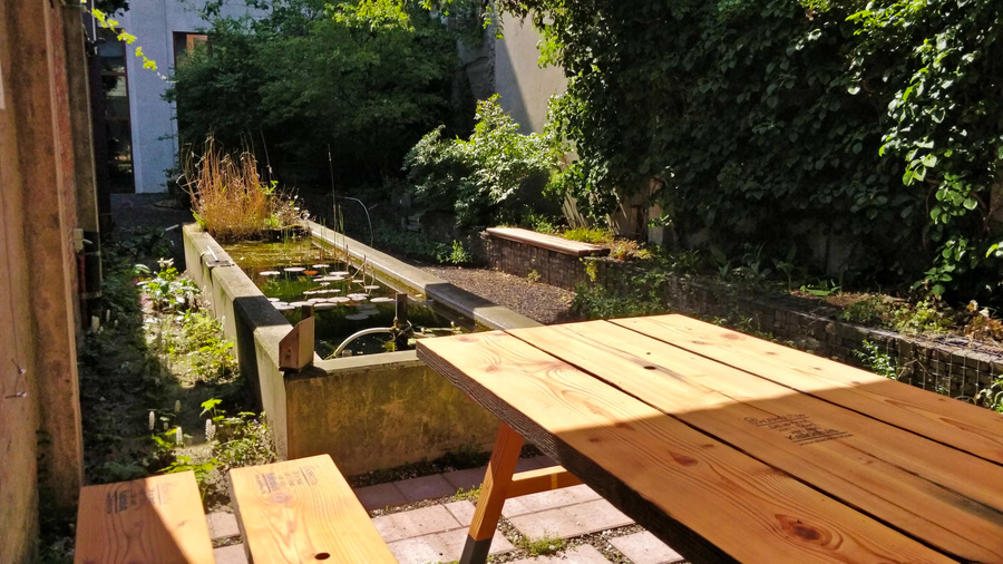 De tafels en banken staan op een terras, naast de vijver.