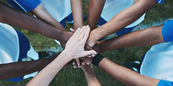 Een groep mensen in sportkleding staat in een cirkel en legt hun handen op elkaar – een krachtig symbool van teamgeest, samenwerking en gedeelde motivatie.