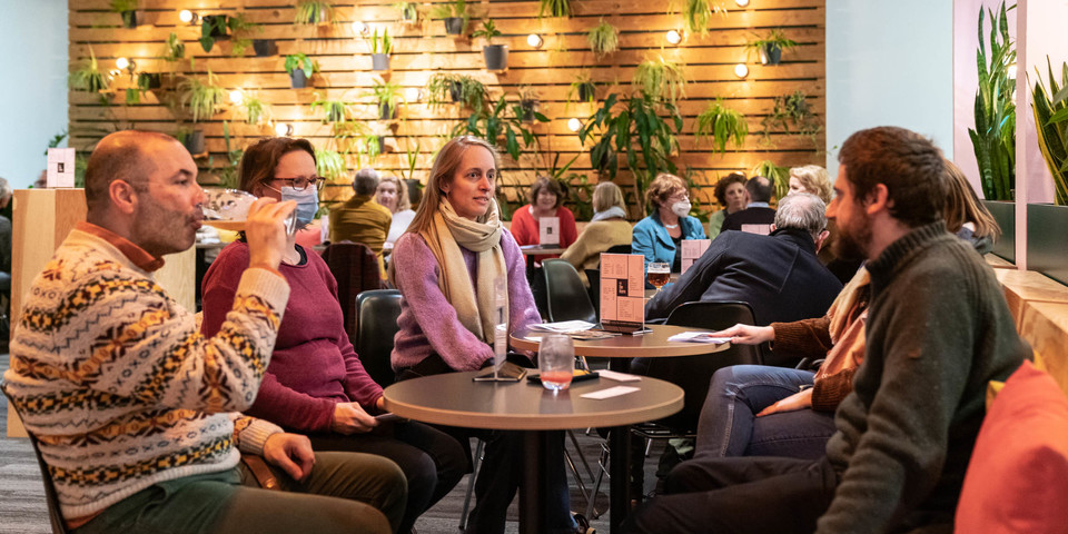 Enkele mensen zitten samen aan een tafeltje in de foyer van Schouwburg De Kern